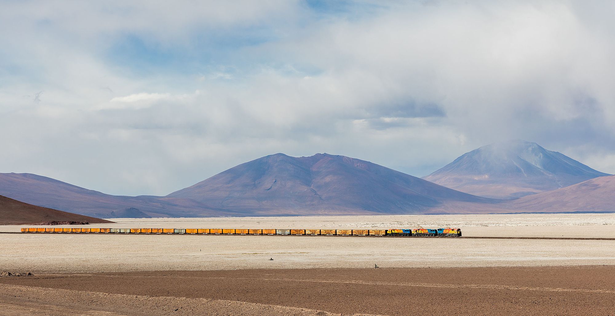FCAB railway crossing the 35 kilometers (22 mi) long route over the west side of the Ascotán salt flat, southwestern Bolivia. The train covers the route Antofagasta - Calama - Ollagüe - Uyuni - La Paz, from 0 metres over the sea level in the coastal city of Antofagasta to over 4,500 metres (14,800 ft) in the area where the picture was taken (exactly in Collahuasi) and has a total length of 1,537 km (955 mi). The locomotives have engines EMD GT22CU-3 2406, Clyde GL26C-2 2009 and Clyde GL26C-2 2004 whereas the Ascotán salt flat has a surface of 246 square kilometers (95 sq mi).