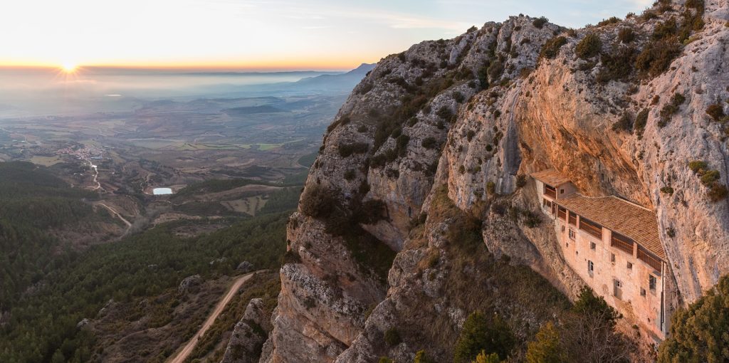 Sunset view of the Ermita de la Virgen de la Peña (Hermitage of the Virgin of the Rock), province of Huesca, Spain. The village of Aniés is seen on the left. The oldest parts of the sanctuary date to Roman times, while much was built in the 13th Century. The hermitage is only accessible on foot, via a steep path in the forest and through caves in the mountain.